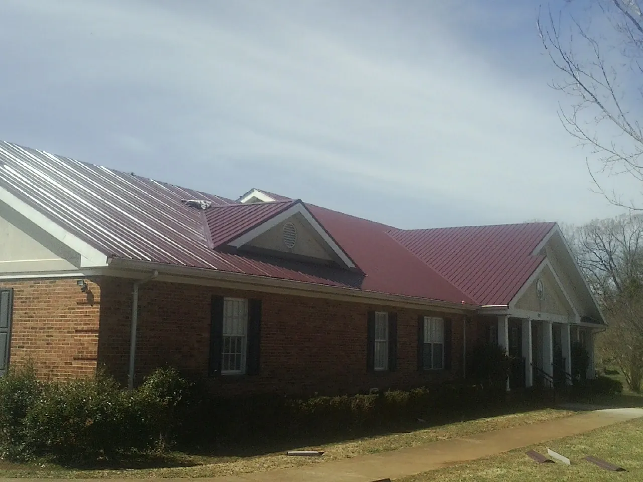 Red metal roof with gabled entries on a long brick building, from a Hail Damage Roof Repair job in Wadena