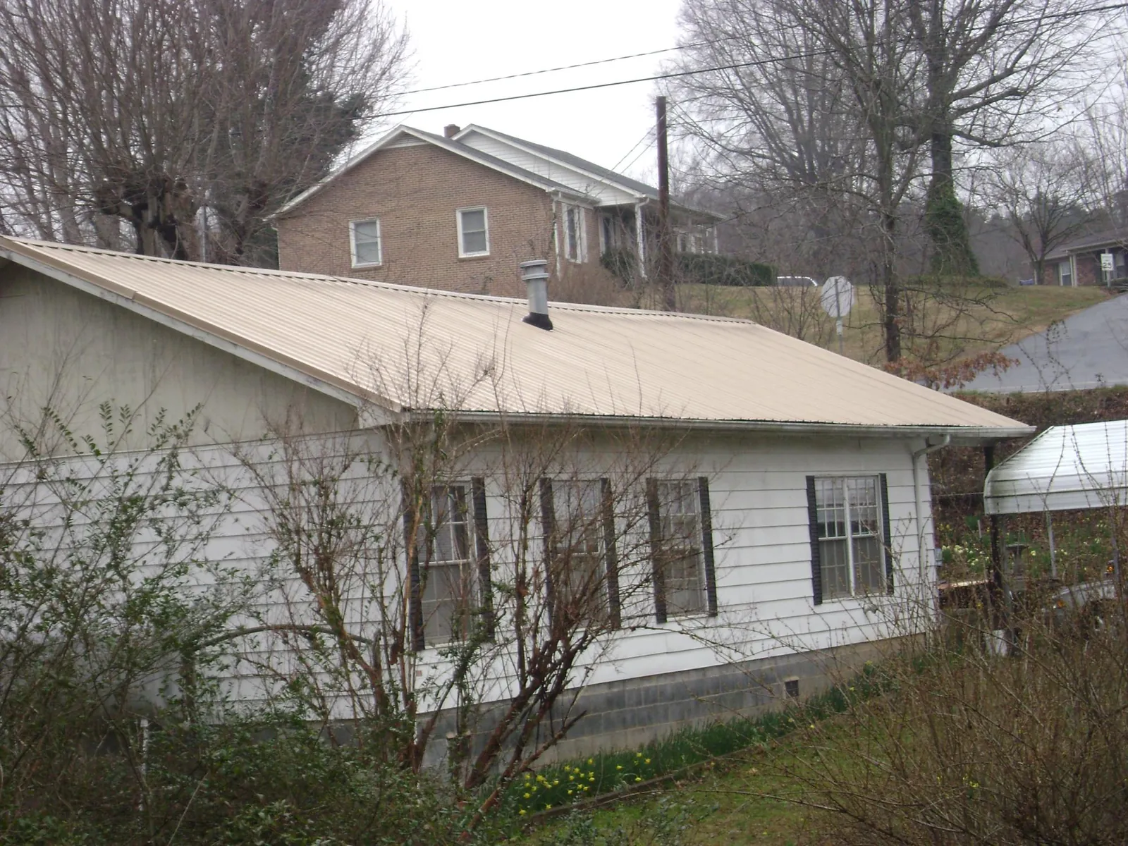 Tan metal roof on a white sided house set into a hillside — Commercial Roofing by Roofing Brothers in Wadena