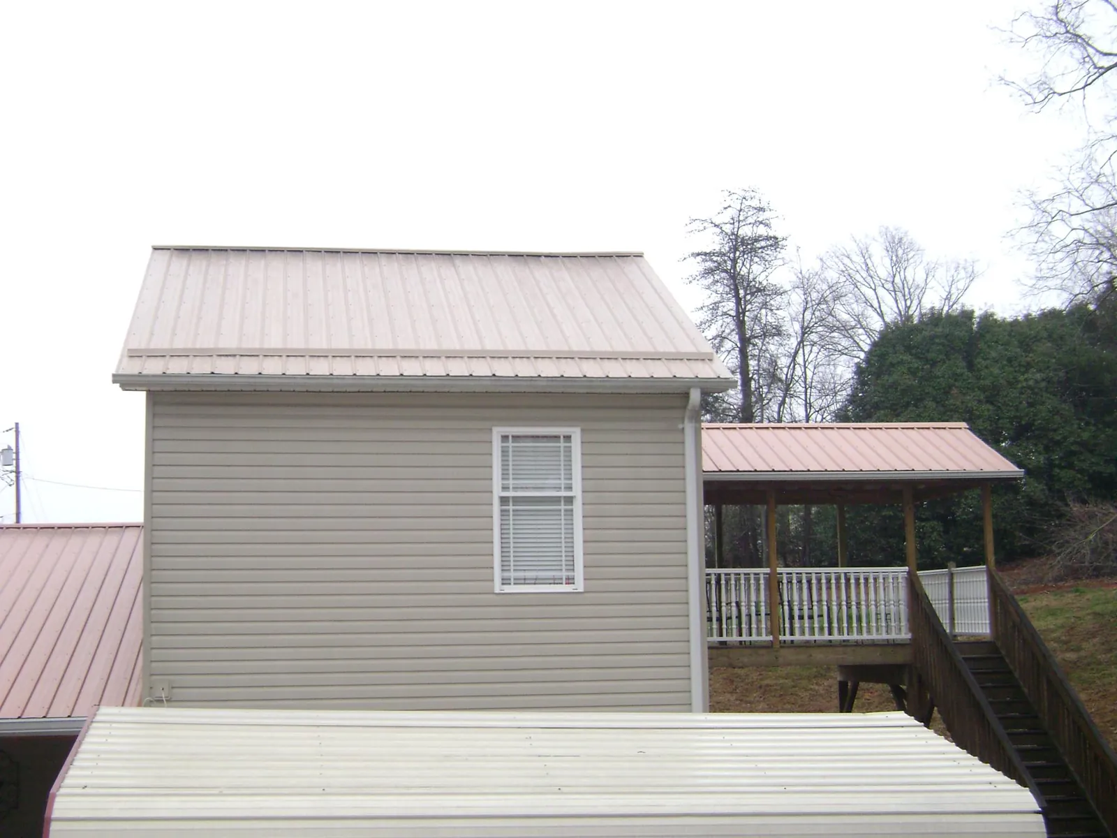 Tan metal roofs on a two story addition and attached porch, from a Roof Replacement job in Wadena